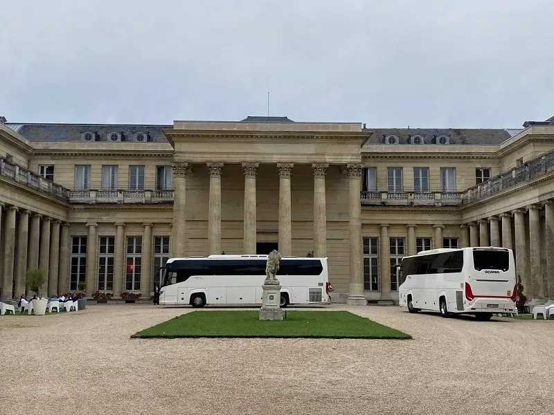 Coach hire Paris services displayed with two stylish white coaches waiting in the courtyard of a grand historic mansion, epitomizing the elegance and convenience of private group transportation in the heart of Paris.