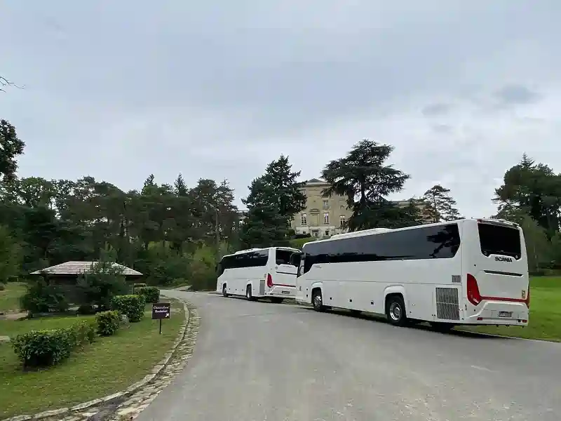 Coach hire Paris services displayed with two stylish white coaches waiting in the courtyard of a grand historic mansion.
