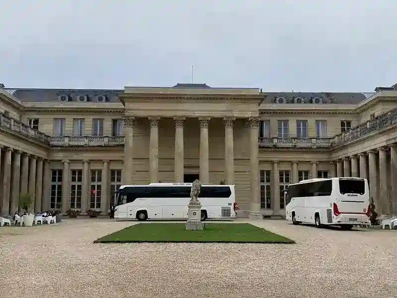 Coach hire Paris services displayed with two stylish white coaches waiting in the courtyard of a grand historic mansion.